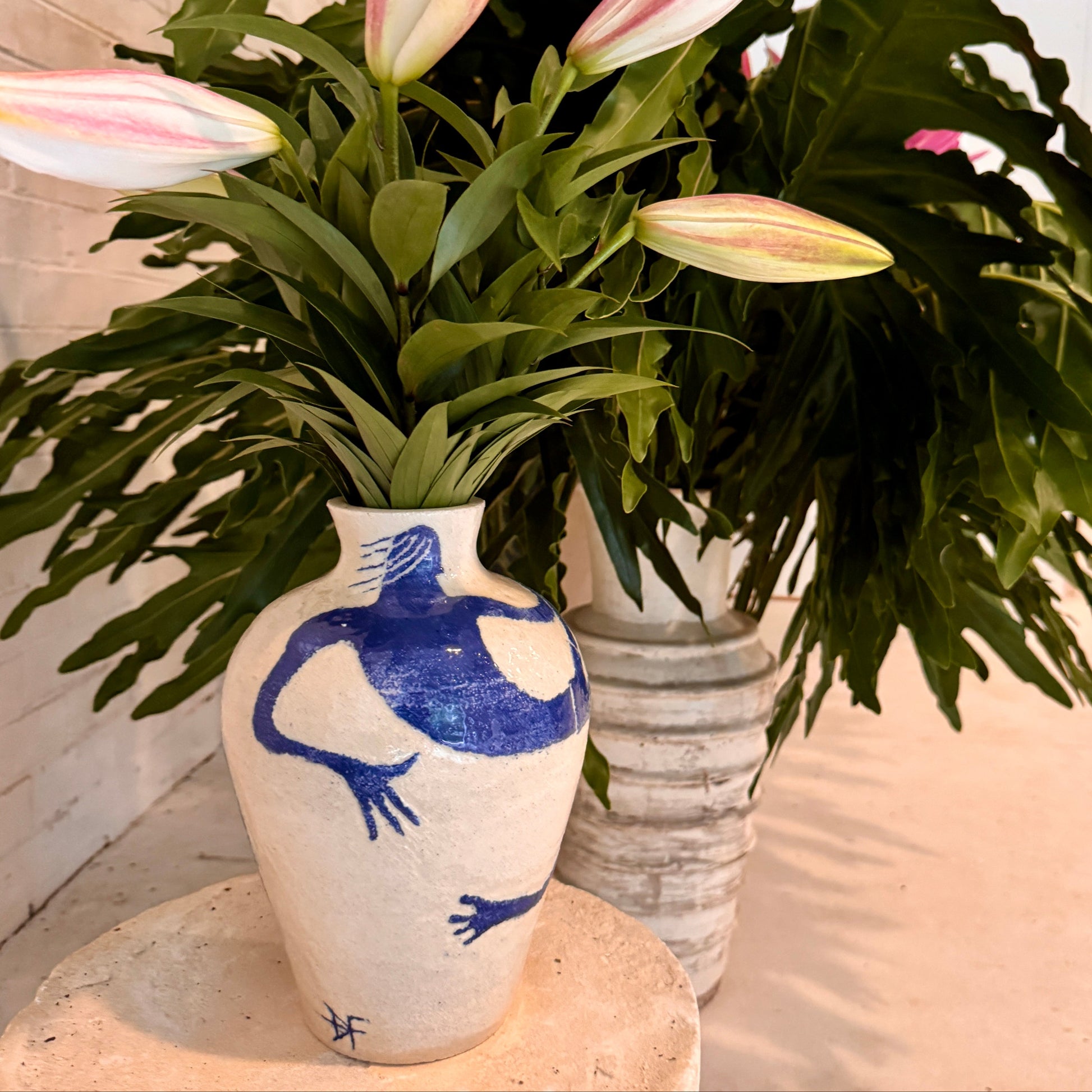vase by famous surf artist Damion Fuller with a blue man design containing green leaves and pink flowers on a light background
