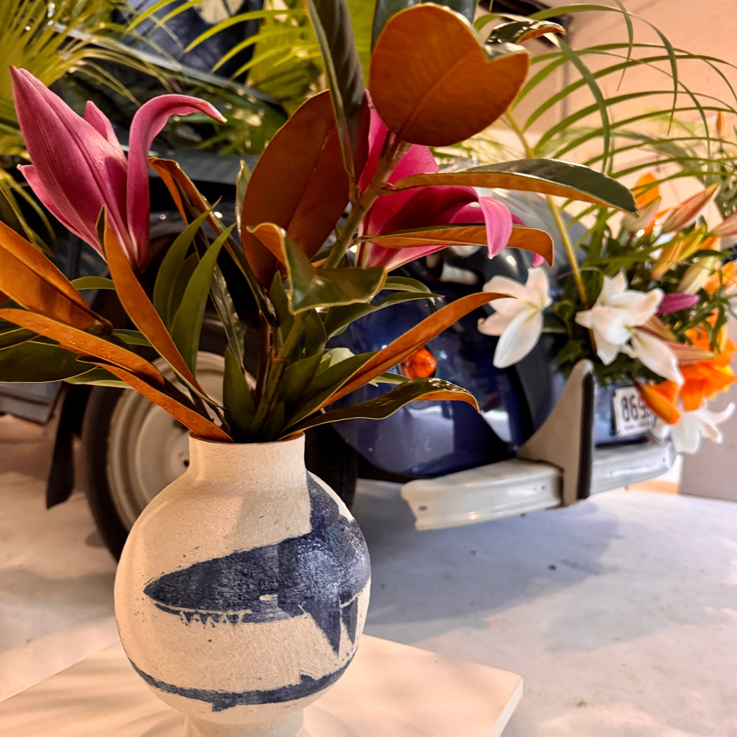 Decorative vase by Damion Fuller with pink flowers and green leaves on a table