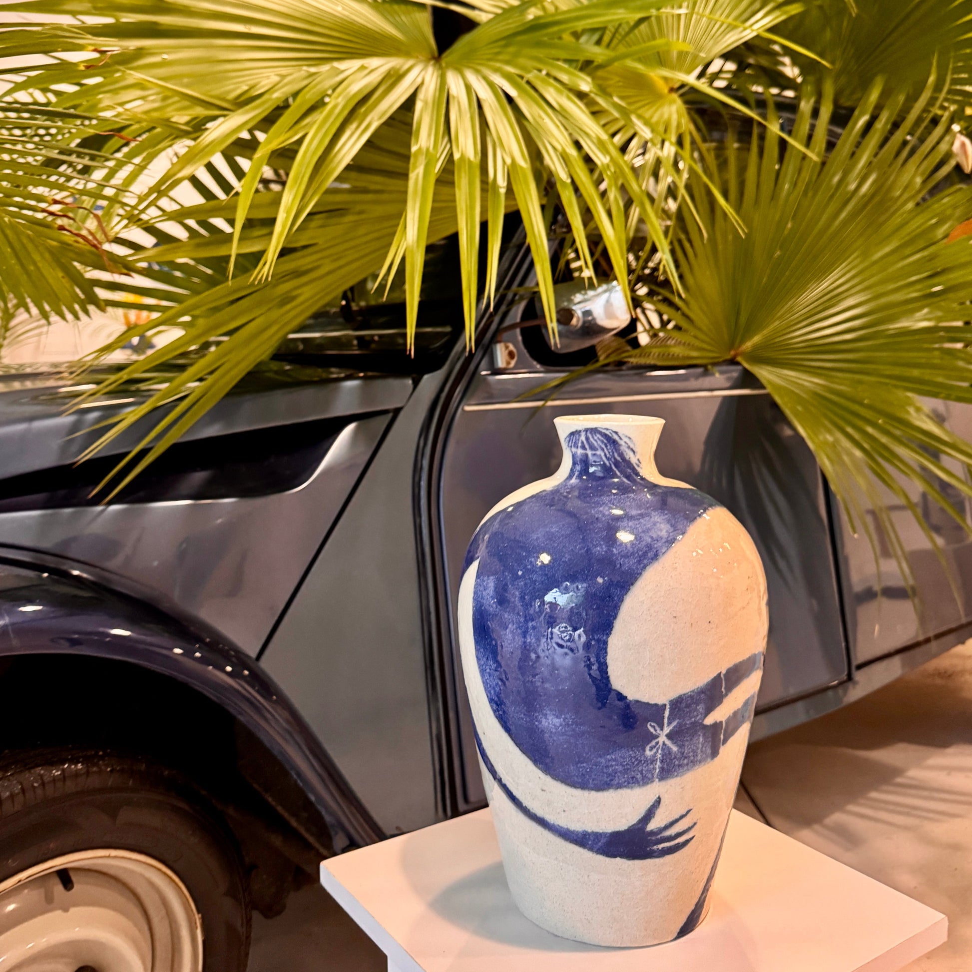 Blue and white ceramic vase by Damion Fuller with artistic design in front of a car