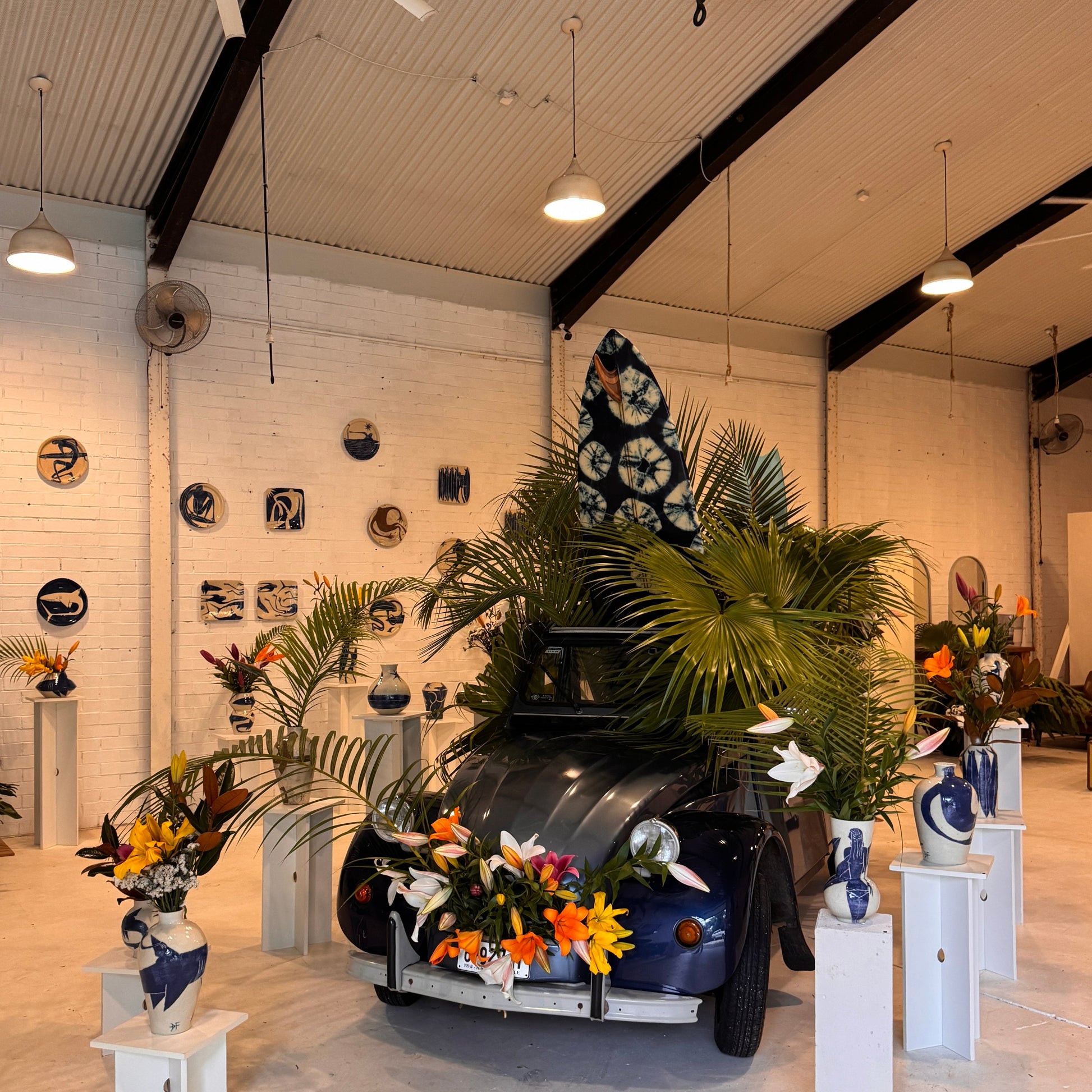 Vintage car displayed indoors with decorative vases by Damion Fuller and plants