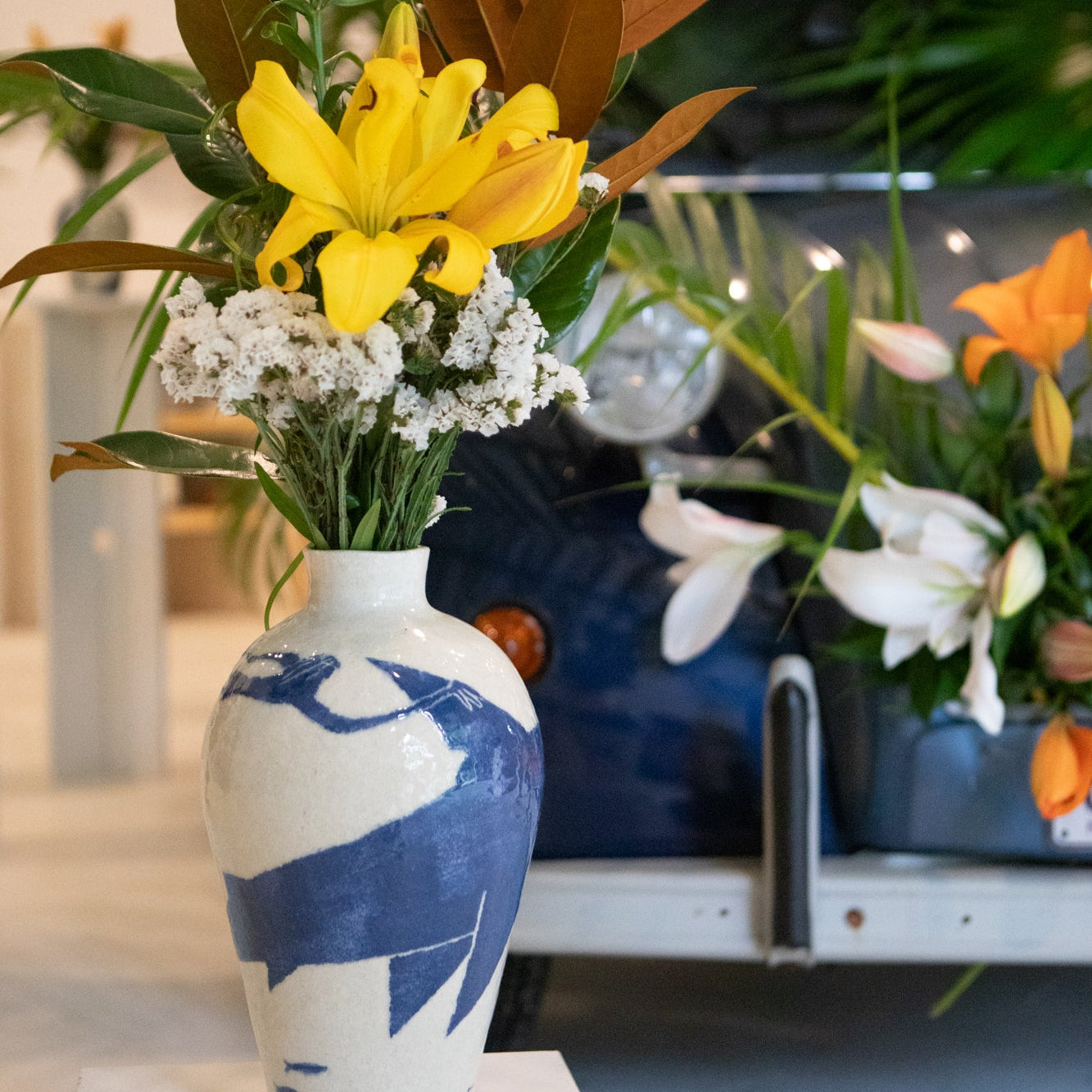 Floral arrangement in a blue and white vase by Damion Fuller with blurred indoor plants in the background