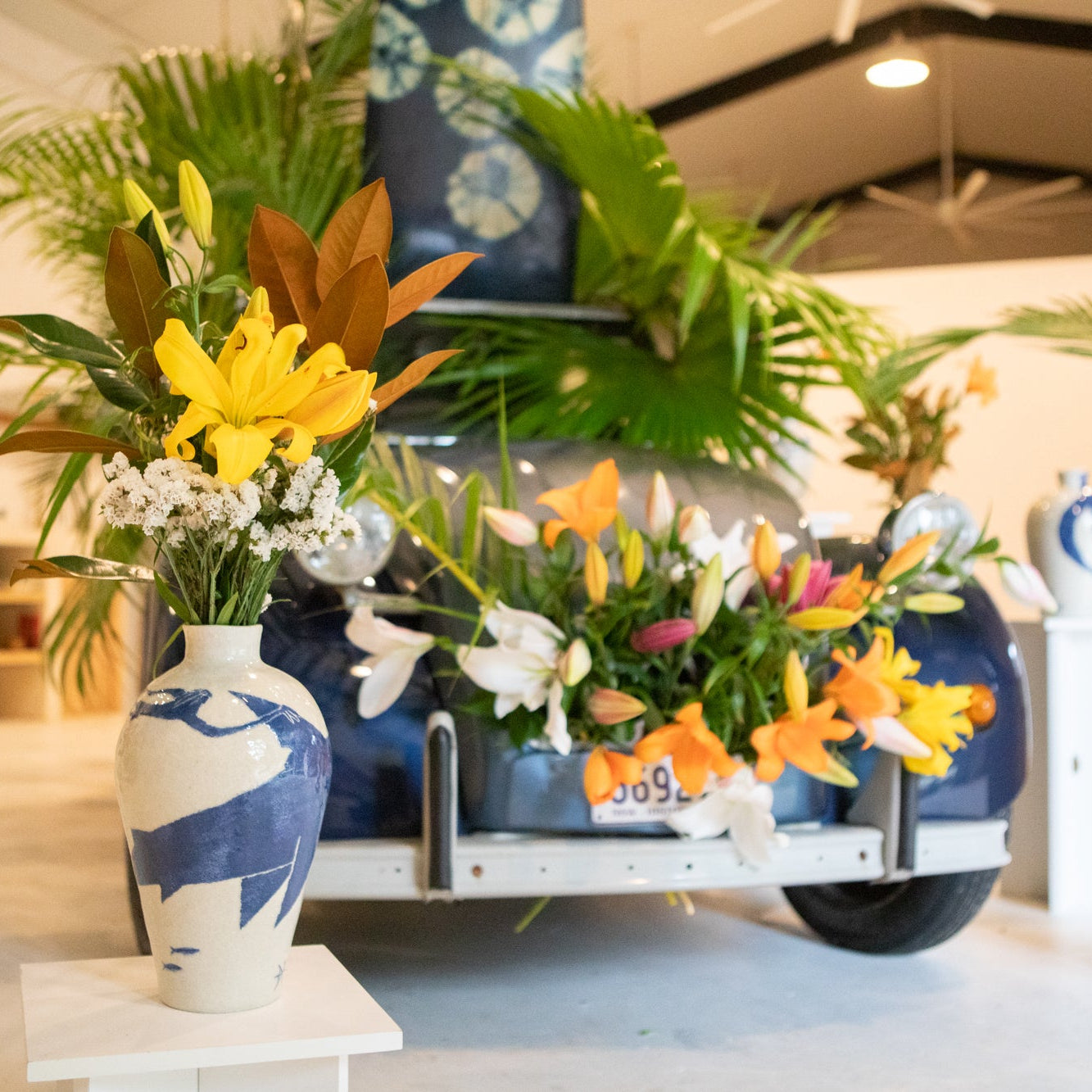 Decorative display with blue and white vases by Damion Fuller,  colorful flowers, and plants in a store setting.